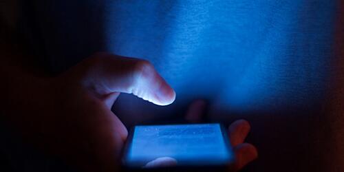 Someone scrolling through a blue mobile phone in the dark
